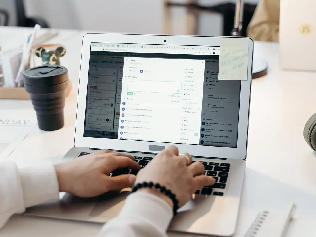 Hands typing on a laptop showing a list of messages, beside a coffee cup.